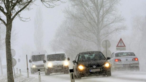 Autos fahren bei starkem Schneefall auf einer Straße.