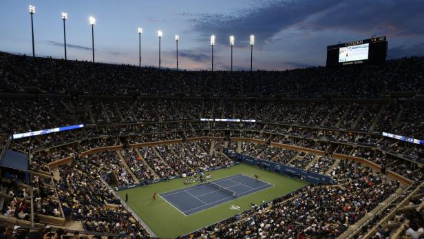 Blick auf ein Tennismatch in einem vollbesetzten Stadion bei Dämmerung.