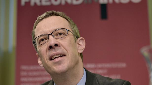 Ein Mann mit Brille spricht vor einem roten Hintergrund.