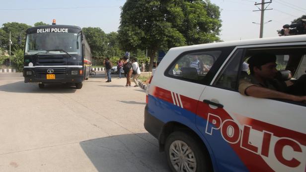 Ein Bus der Delhi Polizei und ein Polizeiauto stehen auf einer Straße.