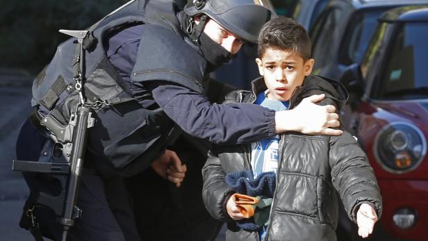 Ein Polizist in Schutzausrüstung begleitet einen Jungen in einer Jacke.