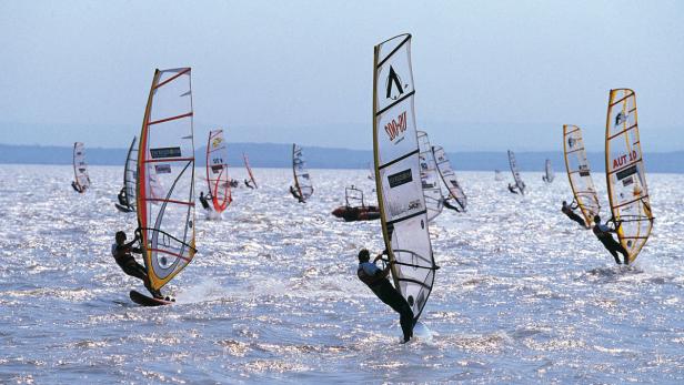 Mehrere Windsurfer sind auf dem Wasser unterwegs.