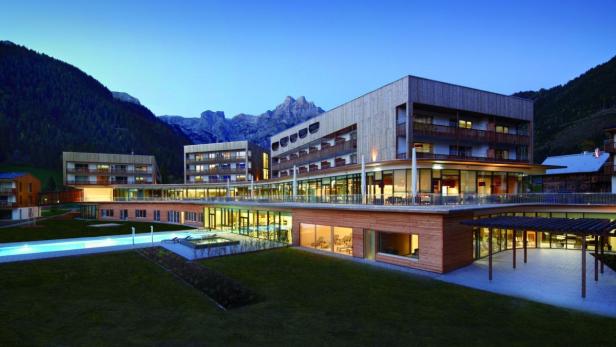 Ein modernes Hotelresort mit Pool liegt vor einer Bergkulisse.