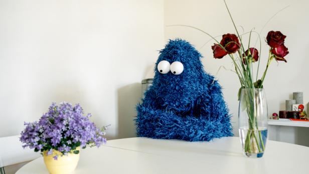 Das Krümelmonster sitzt an einem Tisch mit Blumen und Rosen.