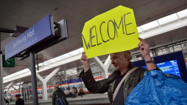 Ein Mann hält ein gelbes Schild mit der Aufschrift „Welcome“ am Salzburger Hauptbahnhof hoch.