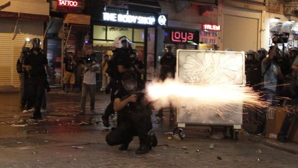 Polizisten in Schutzkleidung feuern mit einer Waffe auf der Straße.