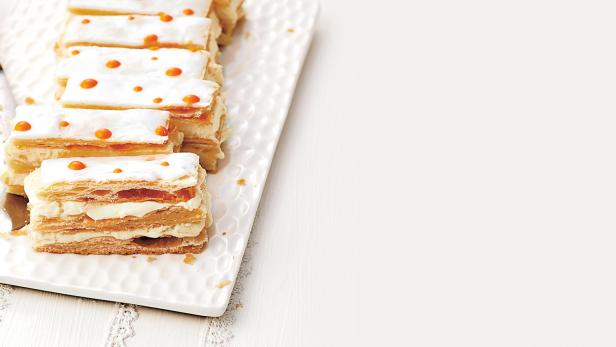 Eine Reihe von Cremeschnitten auf einem weißen Teller mit orangefarbenen Dekorationen.