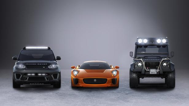 Ein schwarzer Range Rover, ein orangefarbener Jaguar und ein schwarzer Defender stehen nebeneinander.