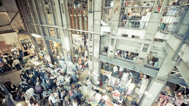 Ein belebter Markt in einer großen Industriehalle mit vielen Menschen und Verkaufsständen.