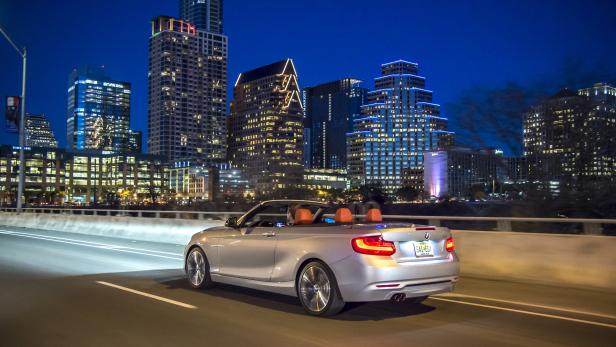 Ein silbernes BMW Cabriolet fährt nachts vor der Skyline einer Stadt.