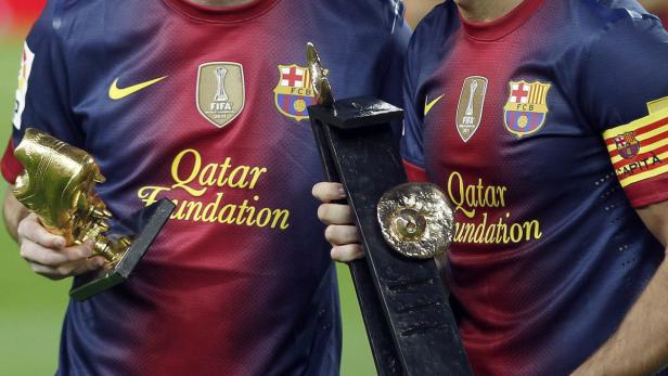 Zwei Fußballspieler des FC Barcelona halten Trophäen in ihren Händen.