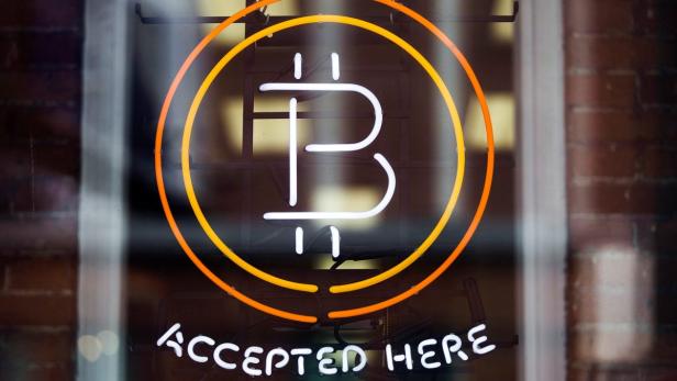 Ein Neon-Schild in einem Fenster zeigt das Bitcoin-Symbol und den Schriftzug „Accepted Here“.