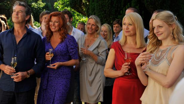 Pierce Brosnan und weitere Personen halten Weingläser bei einer Veranstaltung im Freien.