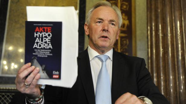 Ein Mann im Anzug präsentiert das Buch „Akte Hypo Alpe Adria“.