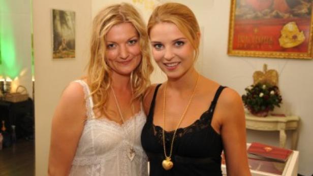 Zwei Frauen posieren nebeneinander, beide tragen Halsketten mit Herzanhängern.