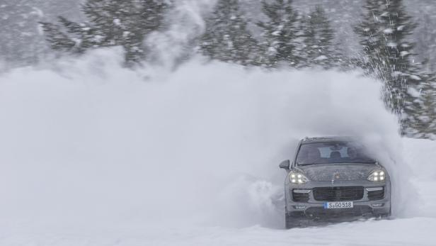 Ein grauer Porsche Cayenne fährt durch eine Schneewehe.