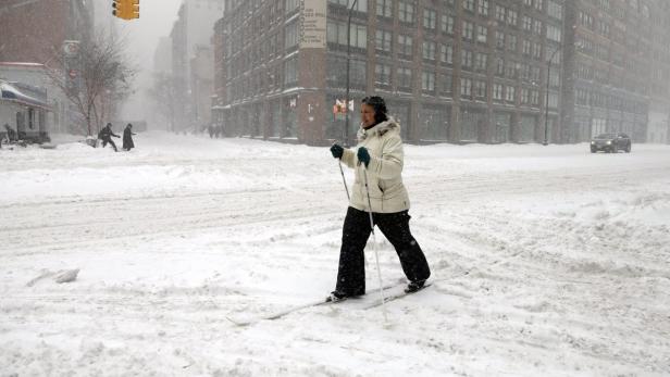 Eine Frau fährt während eines Schneesturms Ski auf einer städtischen Straße.
