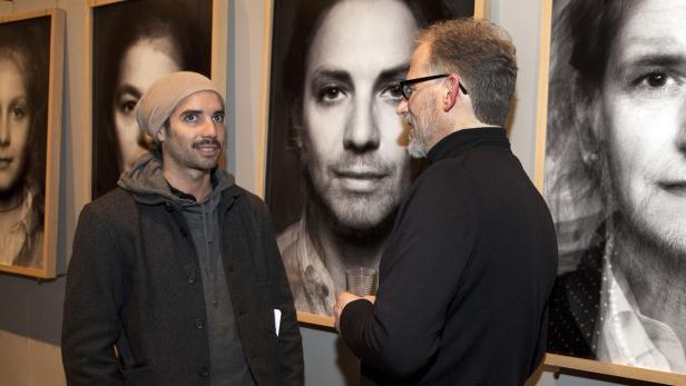 Zwei Männer unterhalten sich in einer Kunstgalerie vor Porträtfotografien.