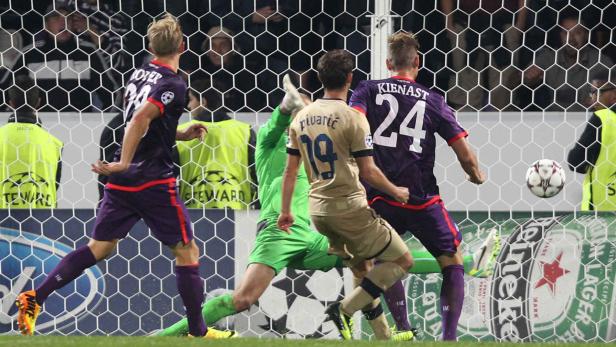 Ein Fußballspiel mit Spielern in lila und beigen Trikots vor einem Tornetz.