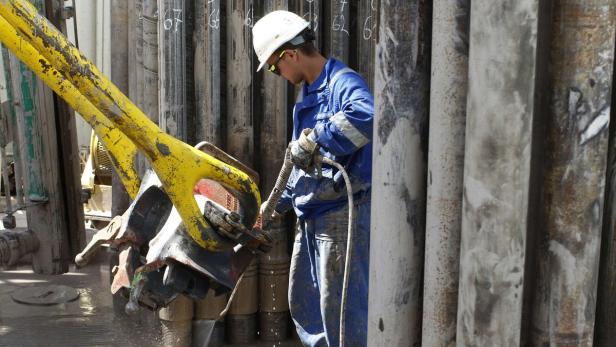 Ein Arbeiter in Arbeitskleidung und Helm bedient eine Bohranlage.