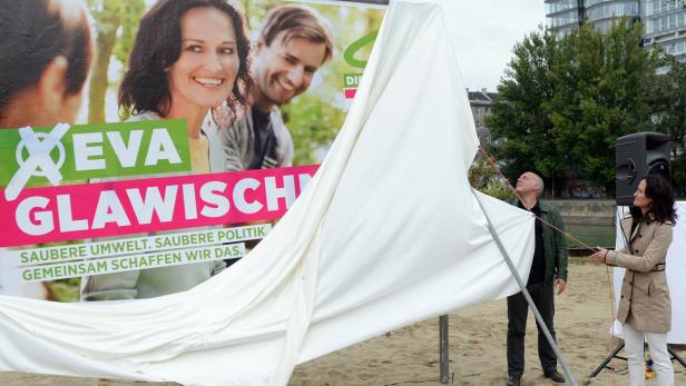 Zwei Personen enthüllen ein Wahlplakat von Eva Glawischnig.