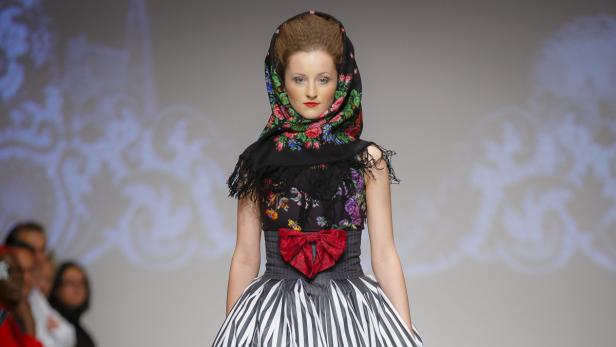 Eine Frau mit einem traditionellen, blumengemusterten Kopftuch und einem gestreiften Rock auf einem Laufsteg.