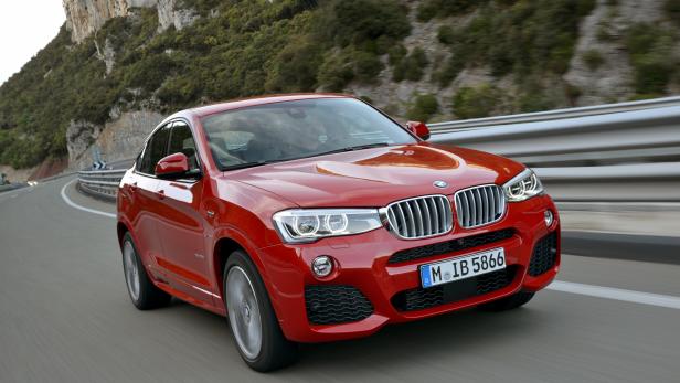 Ein roter BMW X4 fährt auf einer kurvigen Straße entlang einer Felswand.