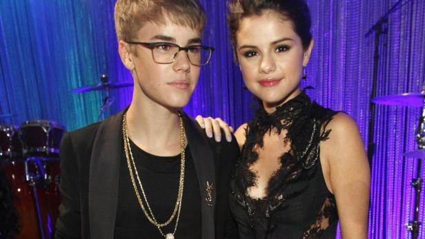 Justin Bieber und Selena Gomez posieren zusammen vor einem lila Vorhang.