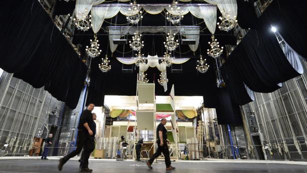 Blick auf eine Theaterbühne mit Dekorationen und Bühnenarbeitern.