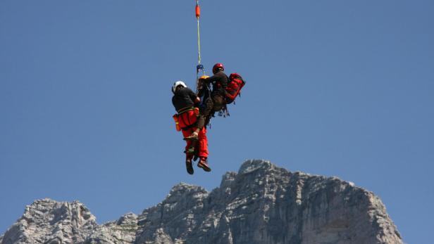 Ein Bergretter seilt eine Person vor einer Bergkulisse ab.