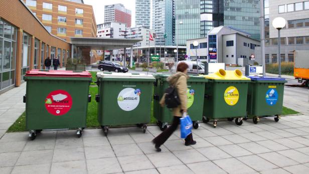 Eine Frau geht an einer Reihe von Müllcontainern für Altpapier, Glas, Plastik und Metall vorbei.