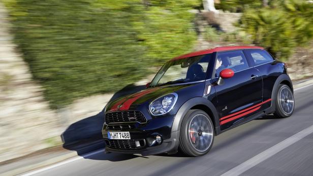 Ein schwarzer Mini Cooper mit roten Streifen fährt auf einer Straße.