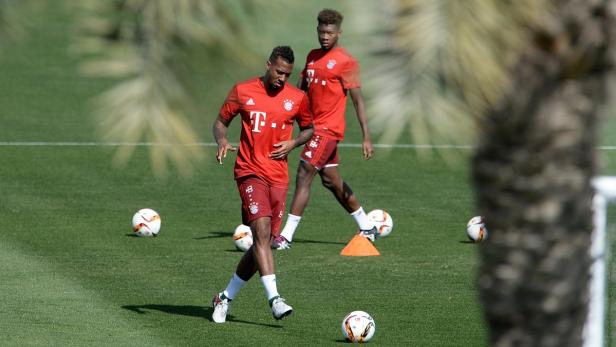 Zwei Fußballspieler des FC Bayern München trainieren auf dem Rasen mit Bällen.