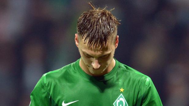 Ein Fußballspieler in einem grünen Trikot mit gesenktem Kopf.