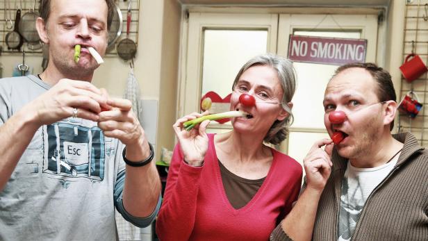 Drei Personen mit roten Nasen essen Gemüse in einer Küche.