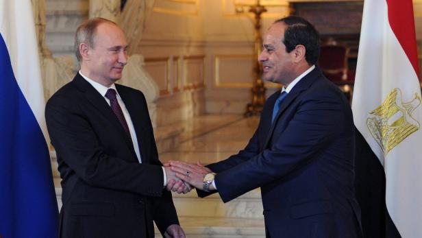 Wladimir Putin und Abdel Fattah El-Sisi schütteln sich die Hände vor russischen und ägyptischen Flaggen.