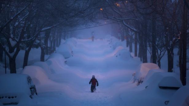 Ein Kind läuft durch eine verschneite Straße, auf der Autos unter Schneemassen begraben sind.