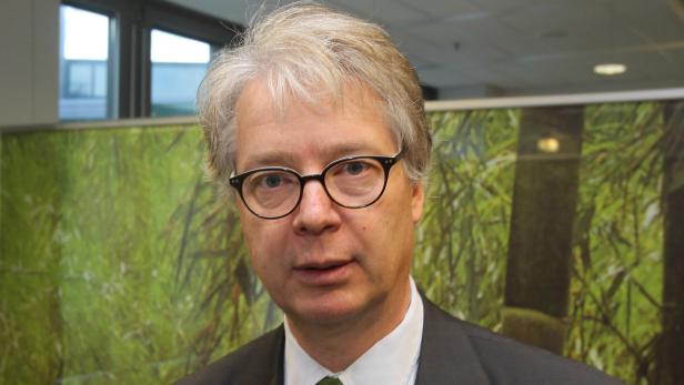 Ein Mann mit Brille und grauem Haar vor einem Hintergrund mit Bambusmotiven.