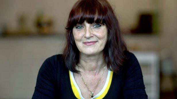 Porträt einer lächelnden Frau mit braunen Haaren und einem schwarzen Oberteil.