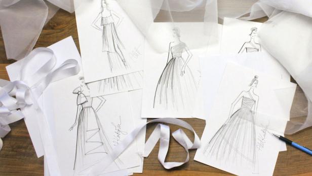 Mehrere Skizzen von Kleiderentwürfen liegen auf einem Tisch.