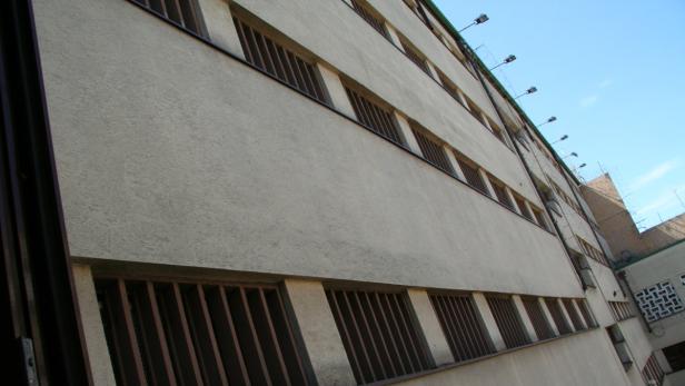 Die Fassade eines Gebäudes mit vergitterten Fenstern und Überwachungsanlagen.