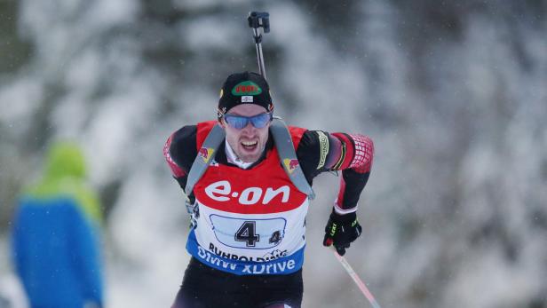 Ein Biathlet läuft mit Skiern und Gewehr auf dem Rücken durch den Schnee.