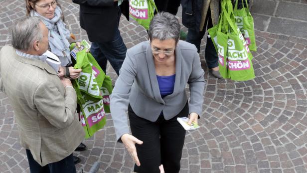 Eine Frau im grauen Blazer verteilt Flyer auf einem gepflasterten Platz.