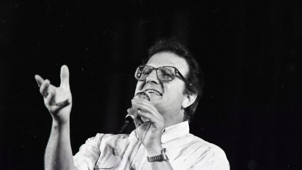 Ein Mann mit Brille singt mit einem Mikrofon in der Hand.