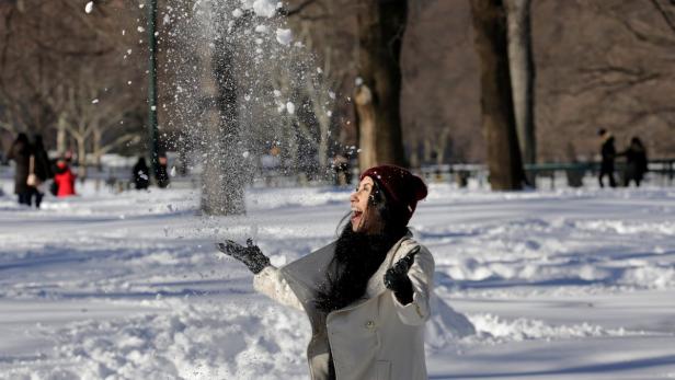 Eine Frau wirft im Winter mit Schnee in die Luft.
