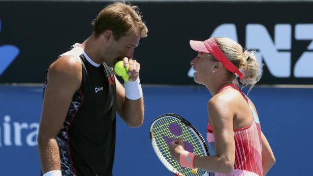 Ein Tennisspieler riecht an einem Tennisball, während eine Tennisspielerin ihn ansieht.