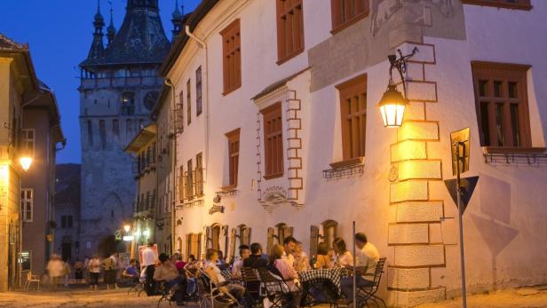 June 2009, Sighisoara, Romania --- People dining in Cetatii Square, with a clock tower in the background, Sighisoara, Romania --- Image by © Marco Cristofori/Corbis
