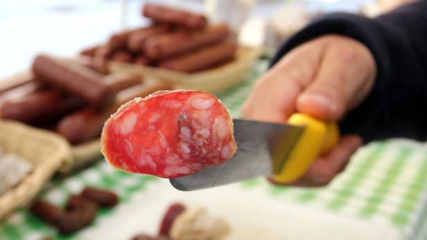 Ein Messer schneidet eine Scheibe Salami.