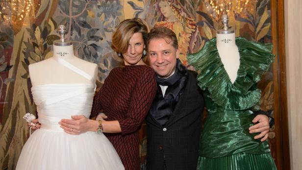 Eine Frau und ein Mann posieren zwischen einem weißen und einem grünen Kleid auf Schneiderpuppen.