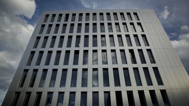 Die Fassade eines modernen Bürogebäudes mit rechteckigen Fenstern spiegelt den Himmel wider.